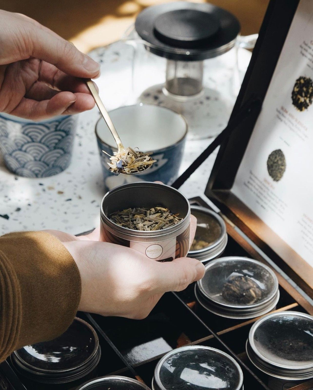 Spooning loose leaf tea from a Kayatea tin beside a wooden tea chest